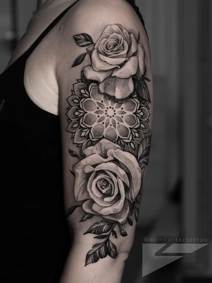 Stipple dotwork mandala framed by black and grey roses on the upper arm